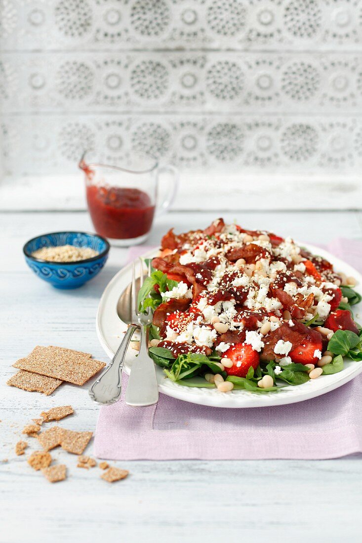 Salad with strawberries, bacon, pearl beans, feta cheese, vegetables and strawberry sauce