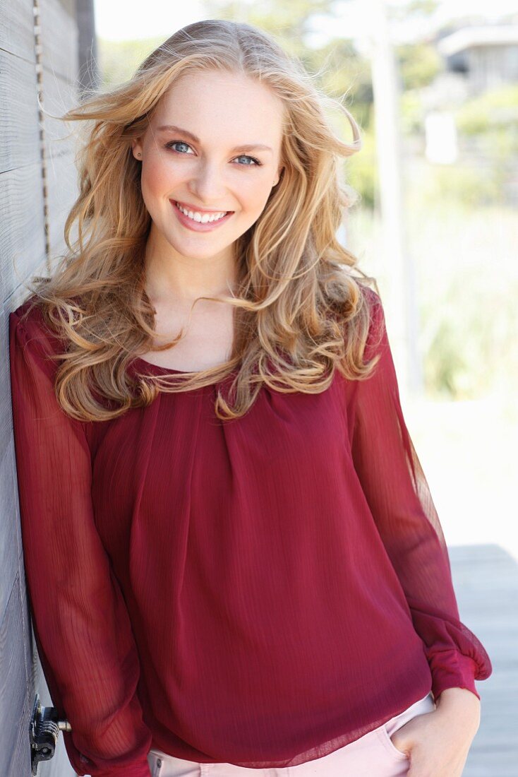 A young dark blonde woman wearing a bordeaux red blouse