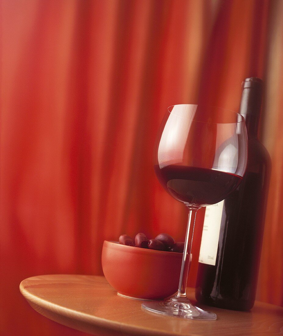 Rotwein und Oliven auf einem Tisch vor rotem Vorhang