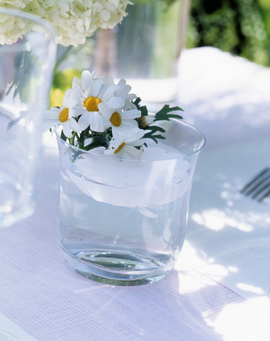 Sommerliche Tischdeko mit Schwimmkerze und Margeritenblüten im Wasserglas