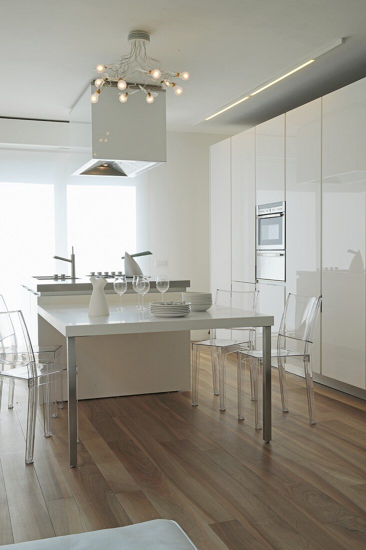 White designer kitchen with extended island counter and plexiglas chairs