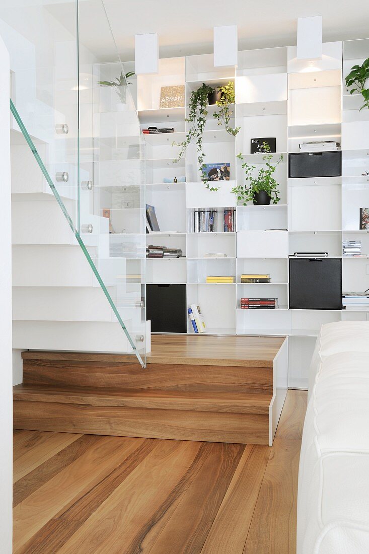 White, fitted, designer shelving and staircase with glass balustrade