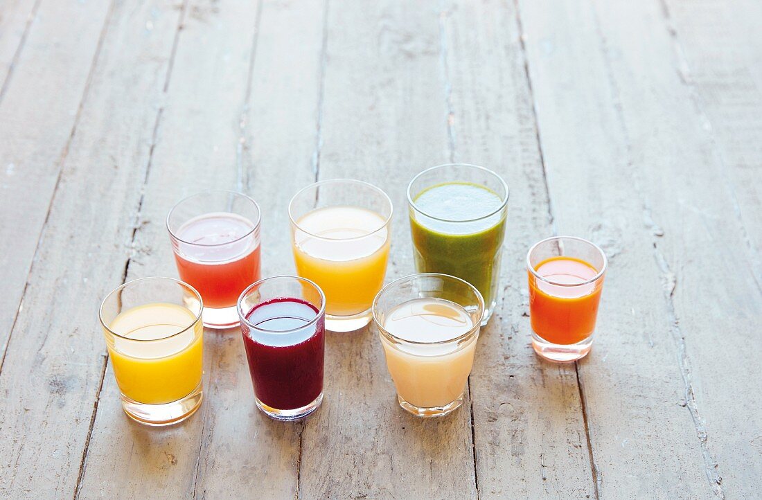 Seven different juices in glasses on a wooden surface