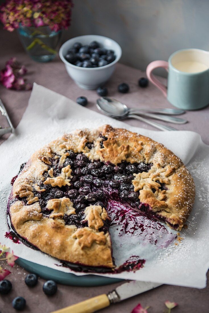 A blueberry galette, sliced, with a jug of cream