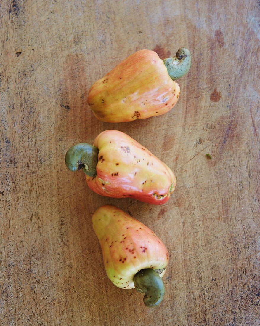 Three cashew apples on a wooden surface