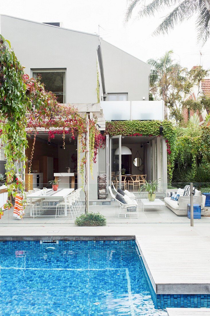 Blue tiled pool and wooden terrace in front of an open apartment building