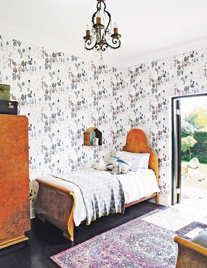 Antique bed in child's bedroom with patterned wallpaper and terrace door