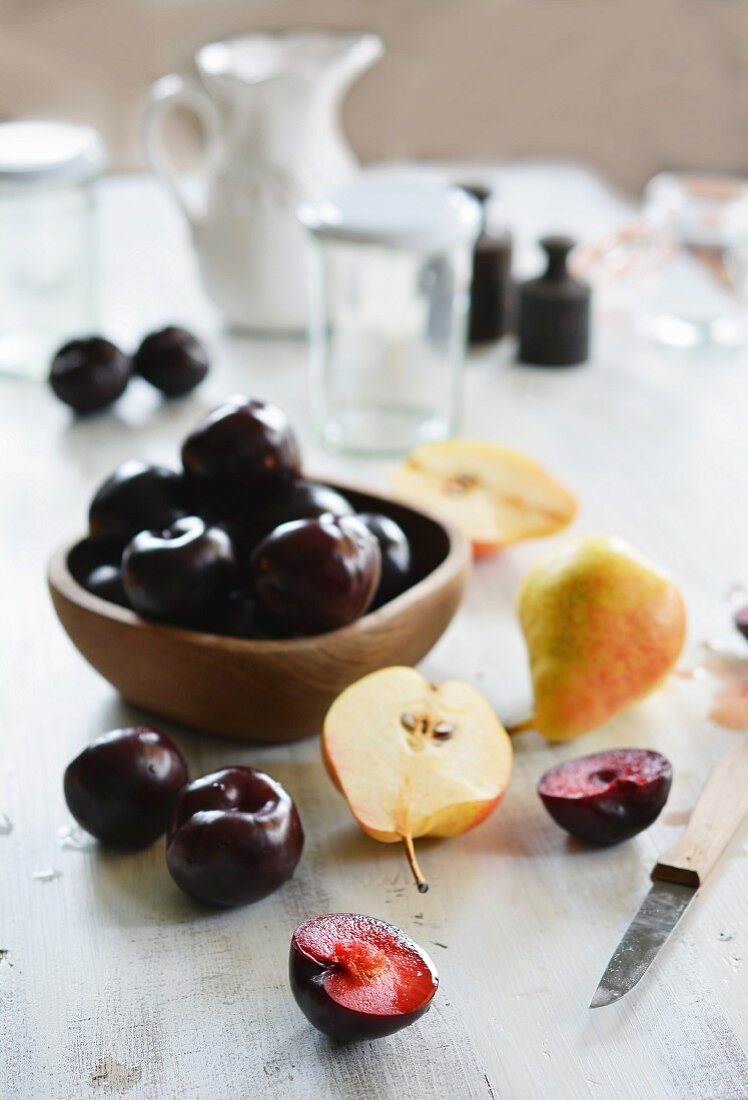 Birnen und Pflaumen auf weißem Holztisch, im Hintergrund leere Marmeladengläser und Gewichte