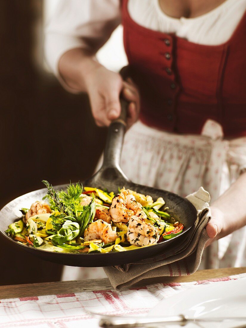 A woman in a traditional dirndl dress serving a dish of giant prawns with herbs