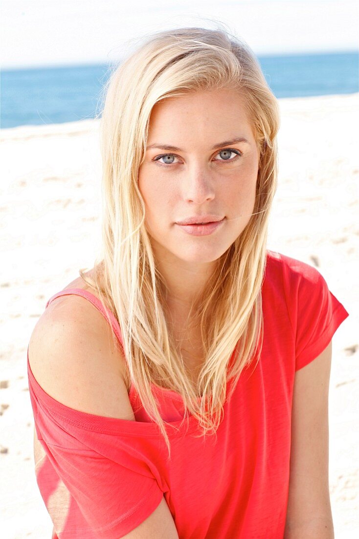 Junge blonde Frau in rotem Top sitzt am Strand