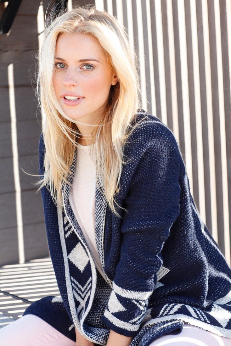 A young blonde woman wearing a top and a blue-and-white cardigan