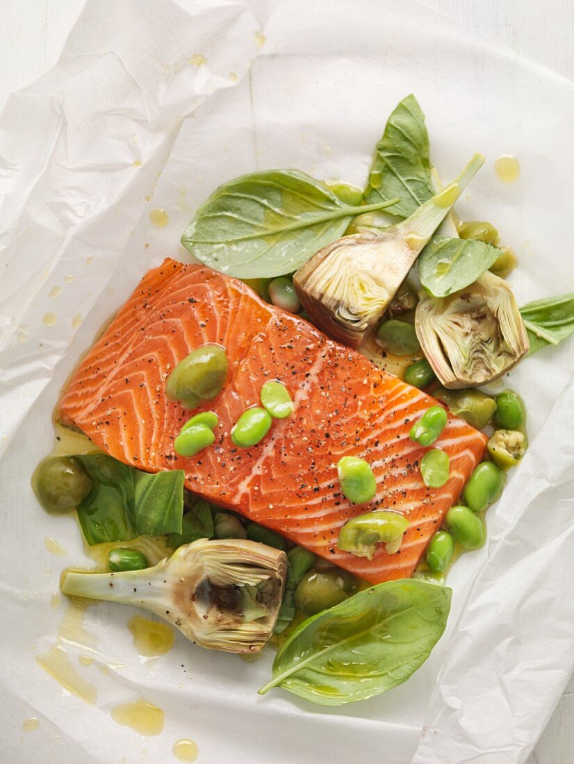 Salmon fillet with artichokes, olives and basil on parchment paper