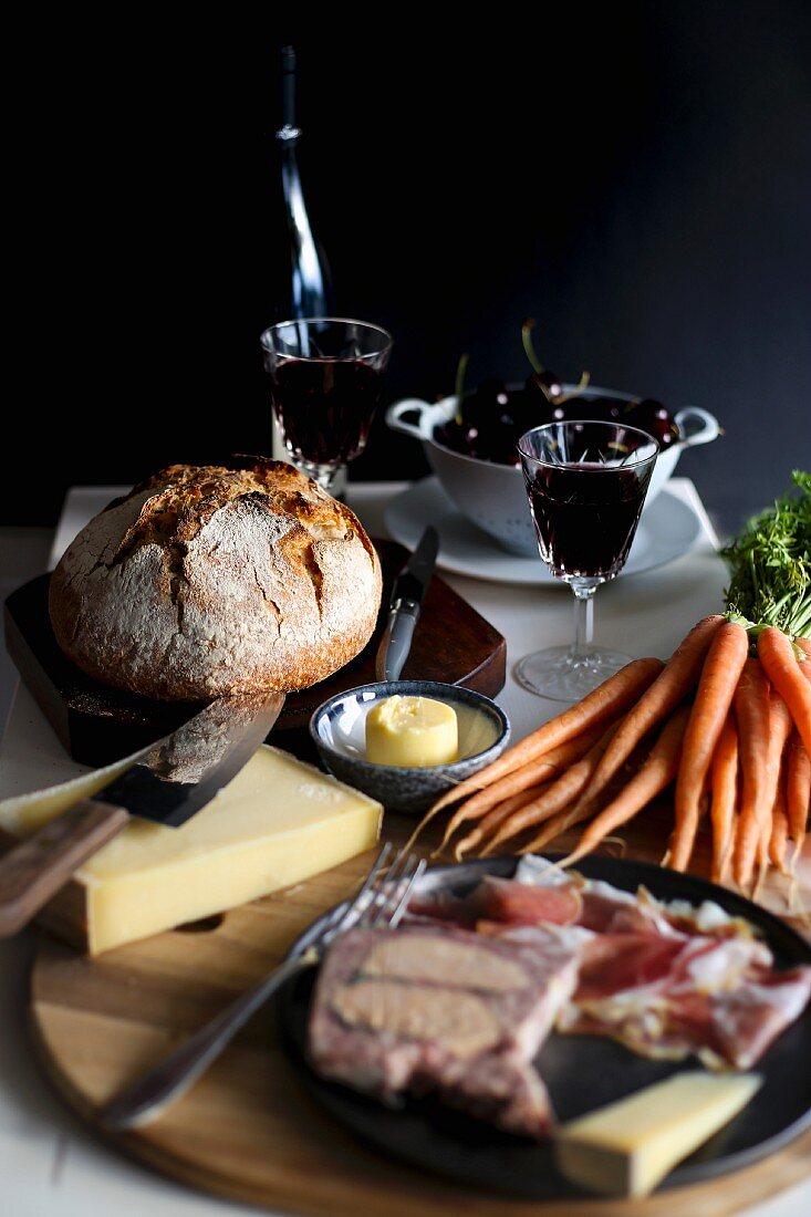 Gedeckter Tisch mit Rotwein, Wurstaufschnitt, Karotten, Butter, Käse und Brot