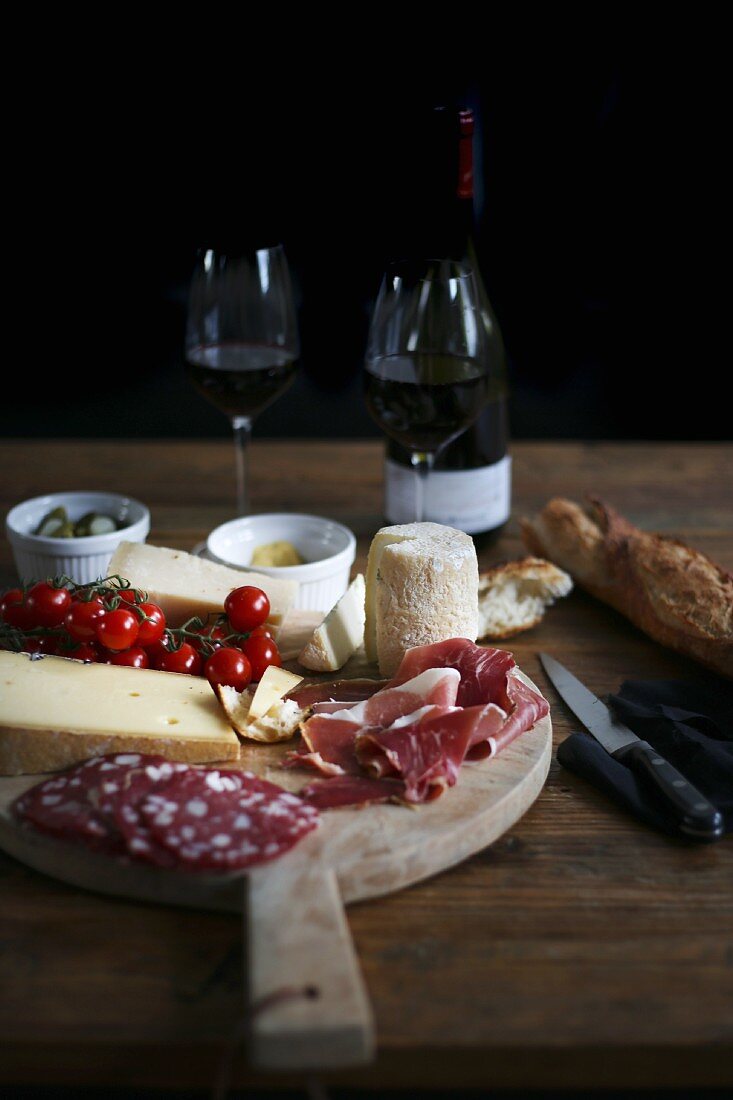 Holzteller mit Schinken, Wurst, Käse, Brot und Rotwein