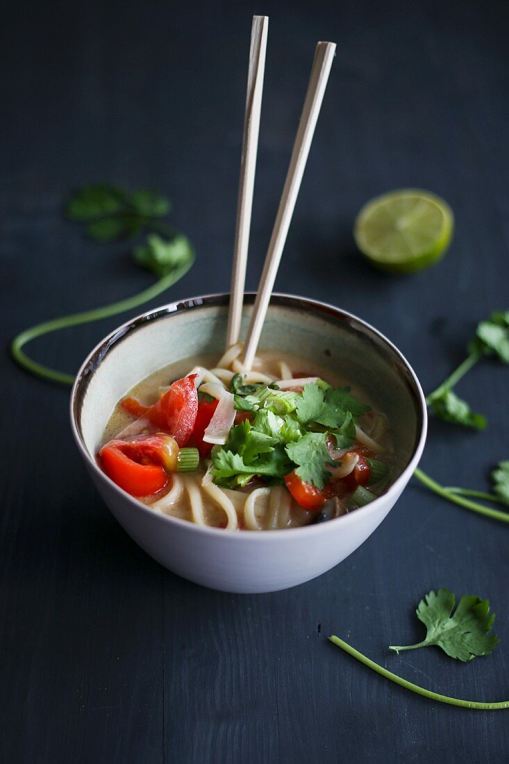 Asian noodle soup with lime, coriander and chopsticks