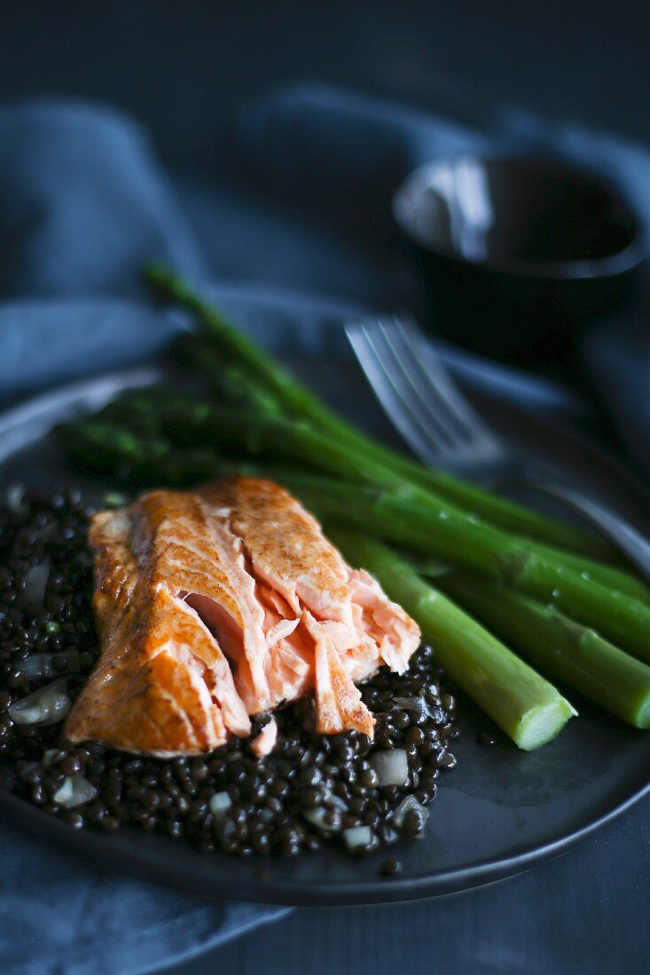Salmon on a bed of black lentils with green asparagus