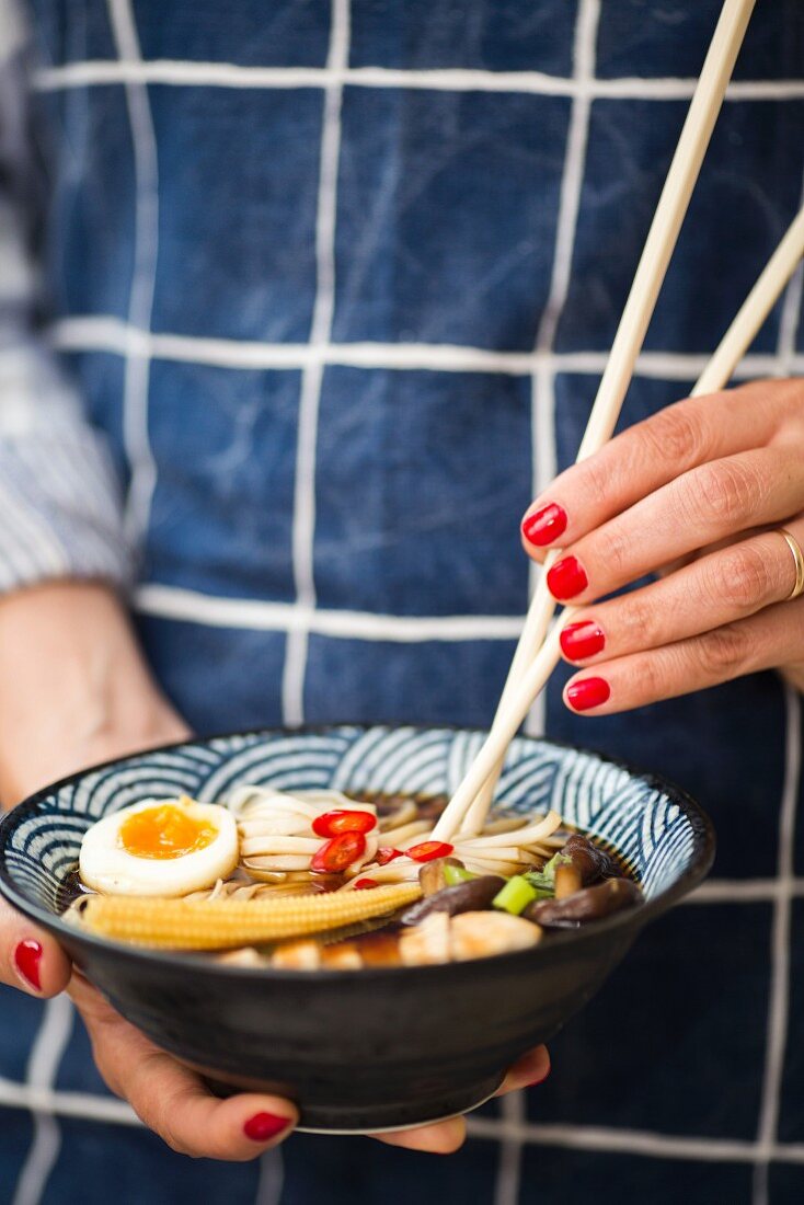A woman's hands holding a bowl of ramen soup