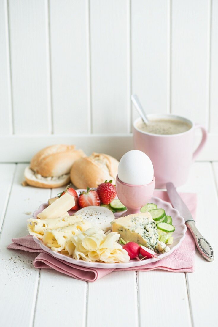 Käsefrühstück mit Ei, Radieschen, Erdbeeren, Gurken, Brötchen und Kaffee