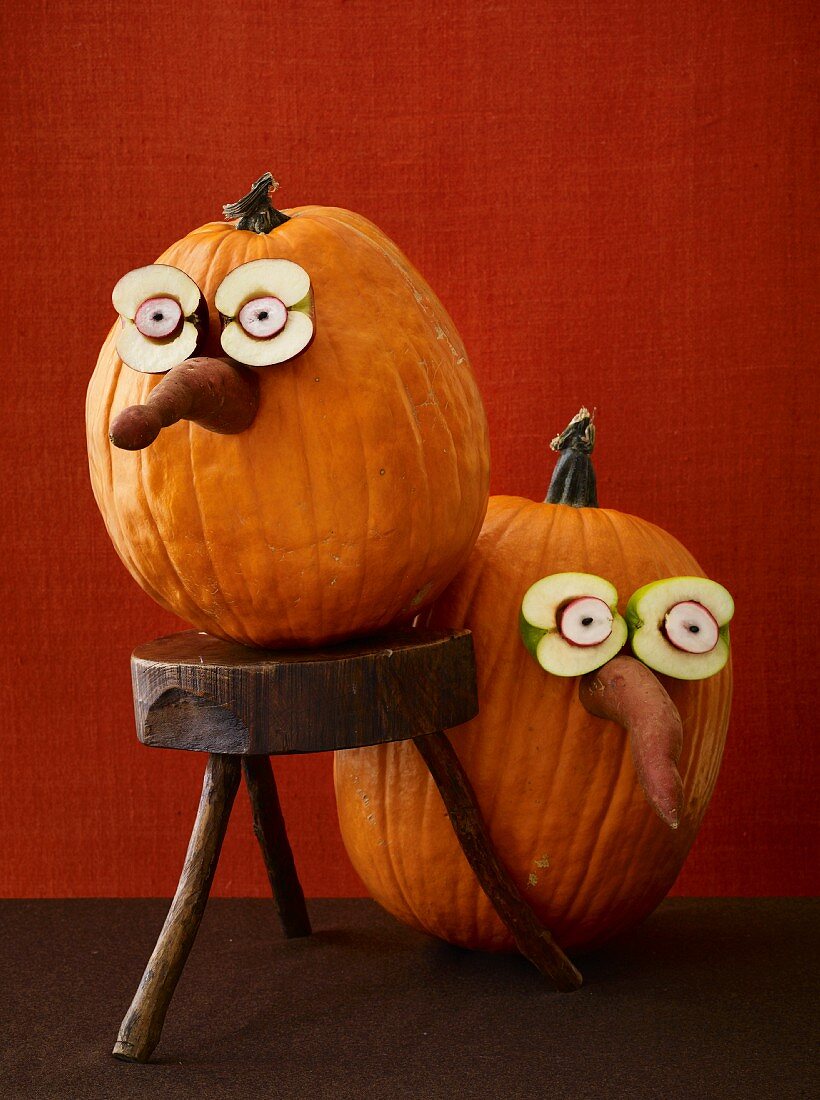 Zwei Halloween-Kürbisse mit lustigen Gesichtern aus Obst und Gemüse