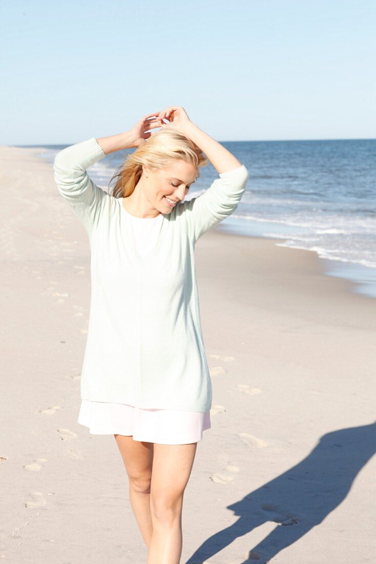 Junge blonde Frau in pastellgrünem Pulli und rosa Minikleid am Strand