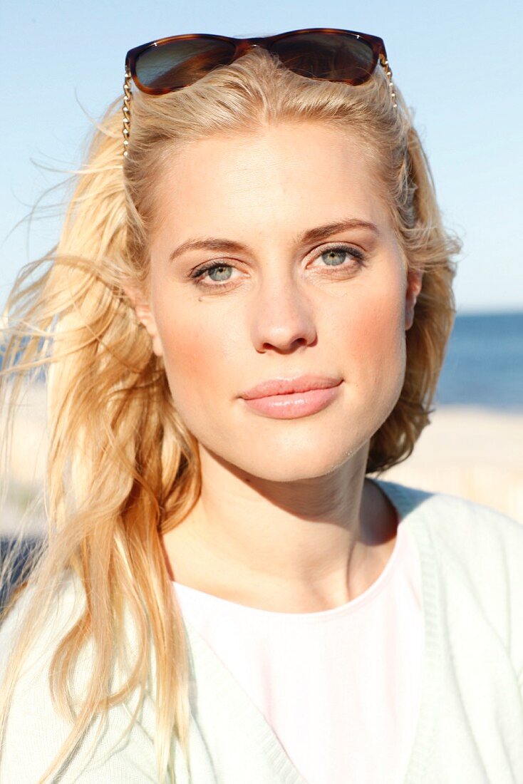A young blonde woman on a beach wearing a pastel green jumper