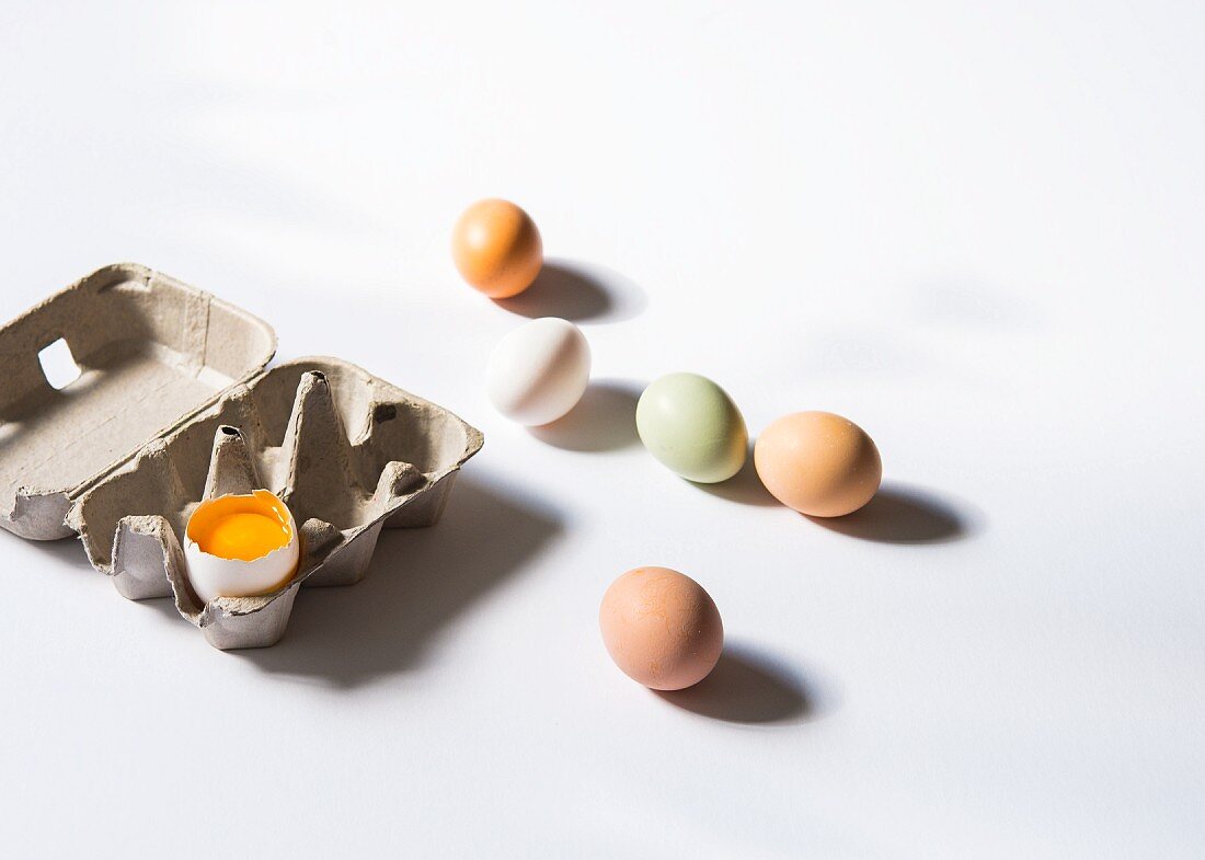 Fresh chicken eggs next to an egg box with a cracked open egg