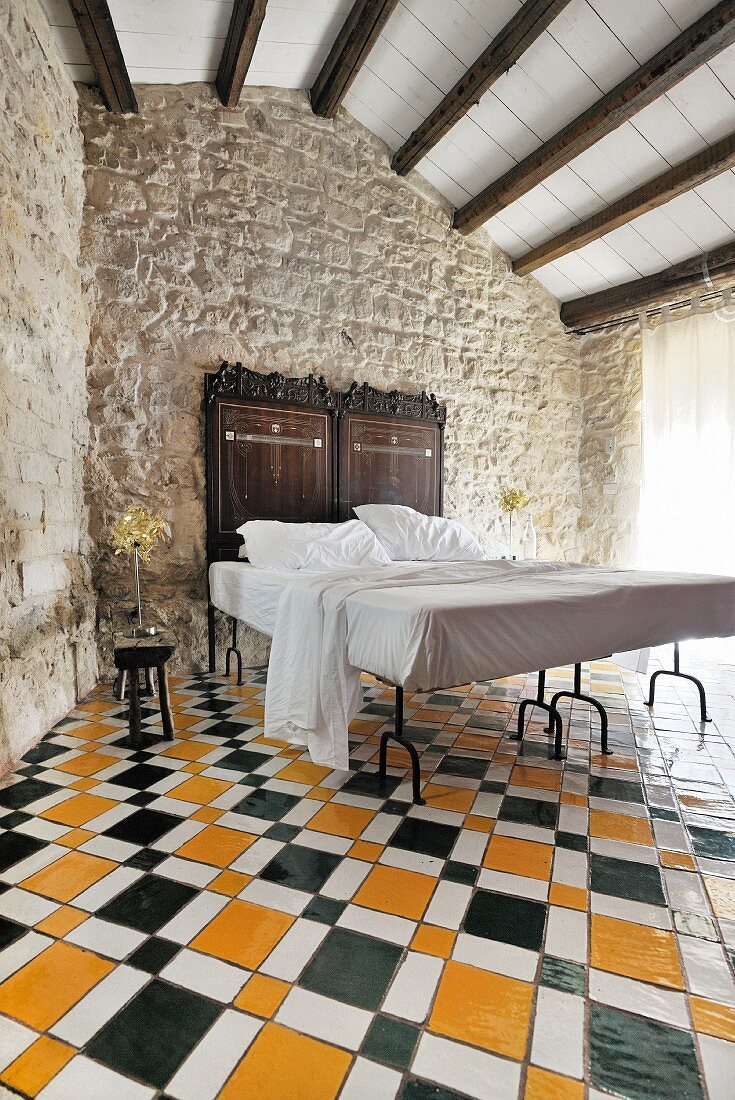 Double bed with antique headboard against traditional stone wall on multicoloured geometric tiled floor