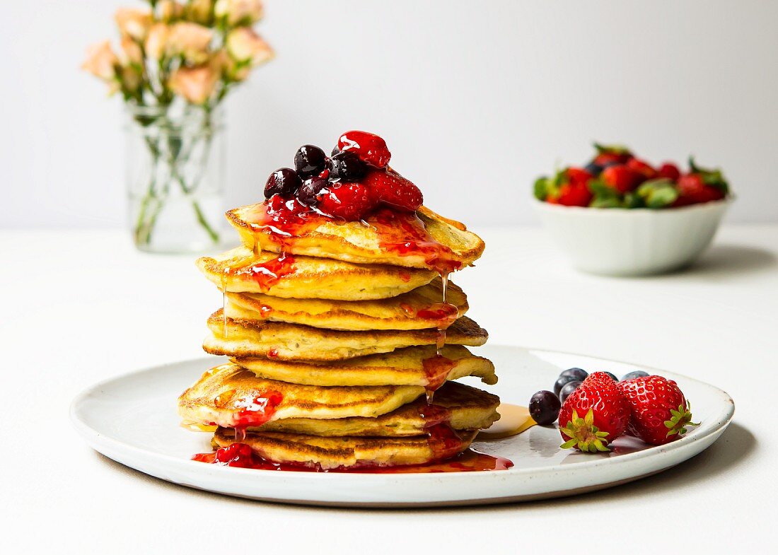 A pile of pancakes with berries and maple syrup