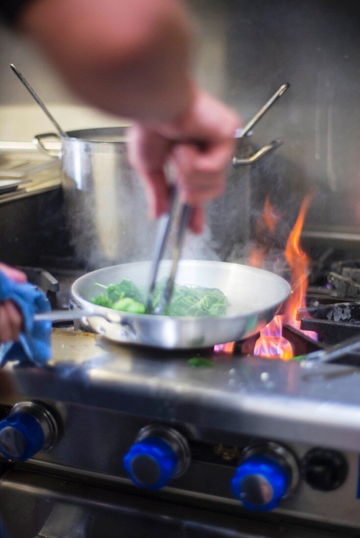 A chef frying vegetables in a pan over the hob
