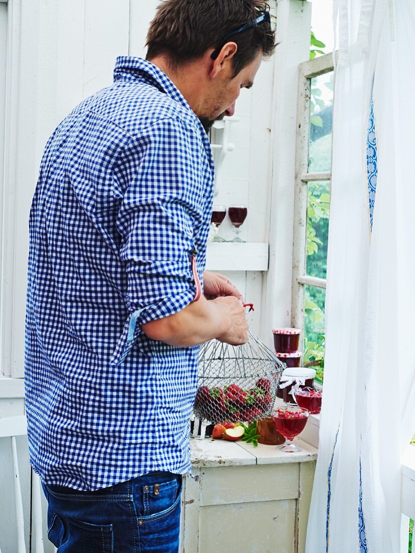 A man with glasses and jars of jam and strawberries in a vintage kitchen