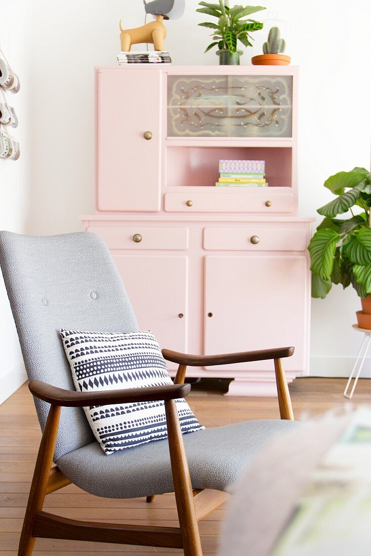 Patterned cushion on retro armchair in front of pink kitchen dresser