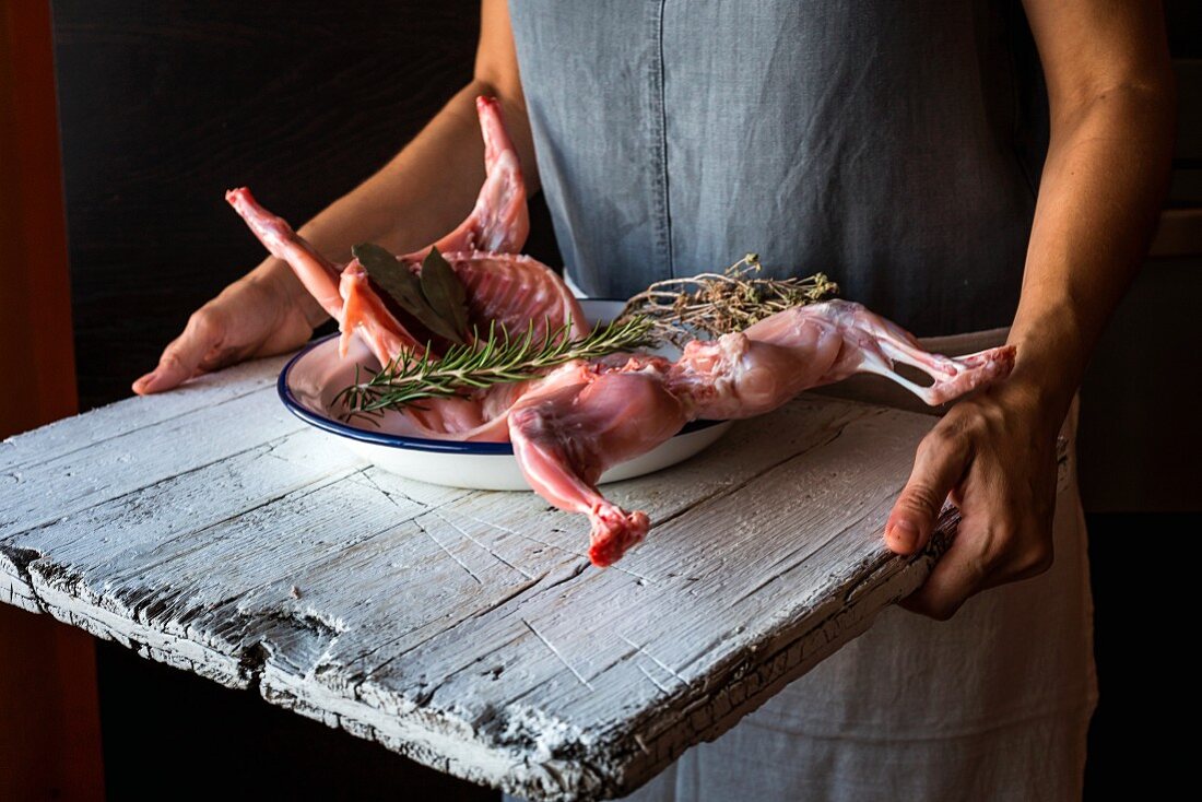 Frau transportiert rohes Kaninchenfleisch auf Holzbrett in Küche