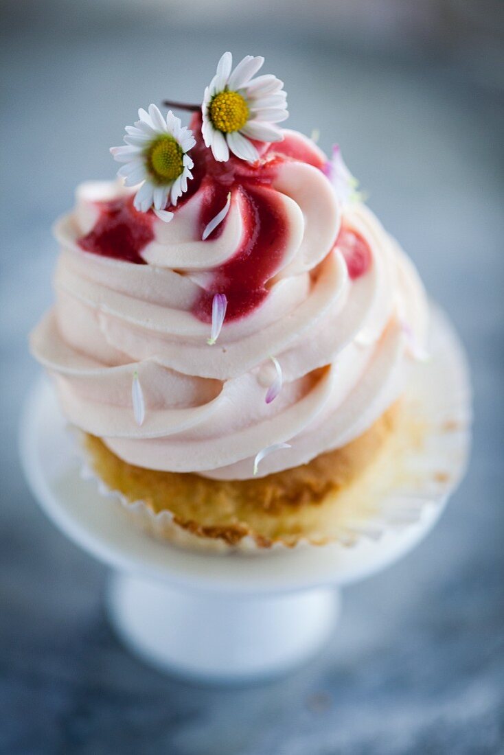 A cupcake with strawberry cream, strawberry sauce, and daisies