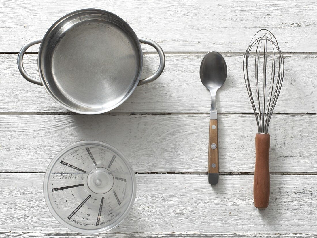 Kitchen utensils: a saucepan, measuring cup, spoon and whisk