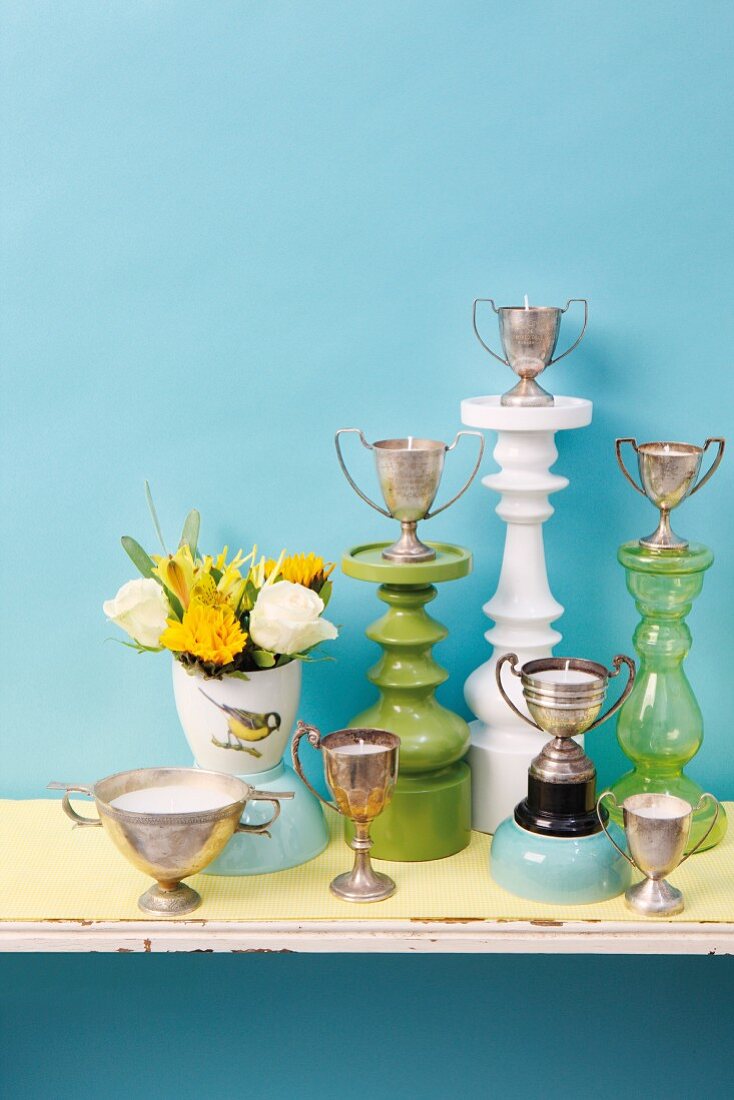 DIY candles poured into silver trophies and decoratively arranges against pale blue wall
