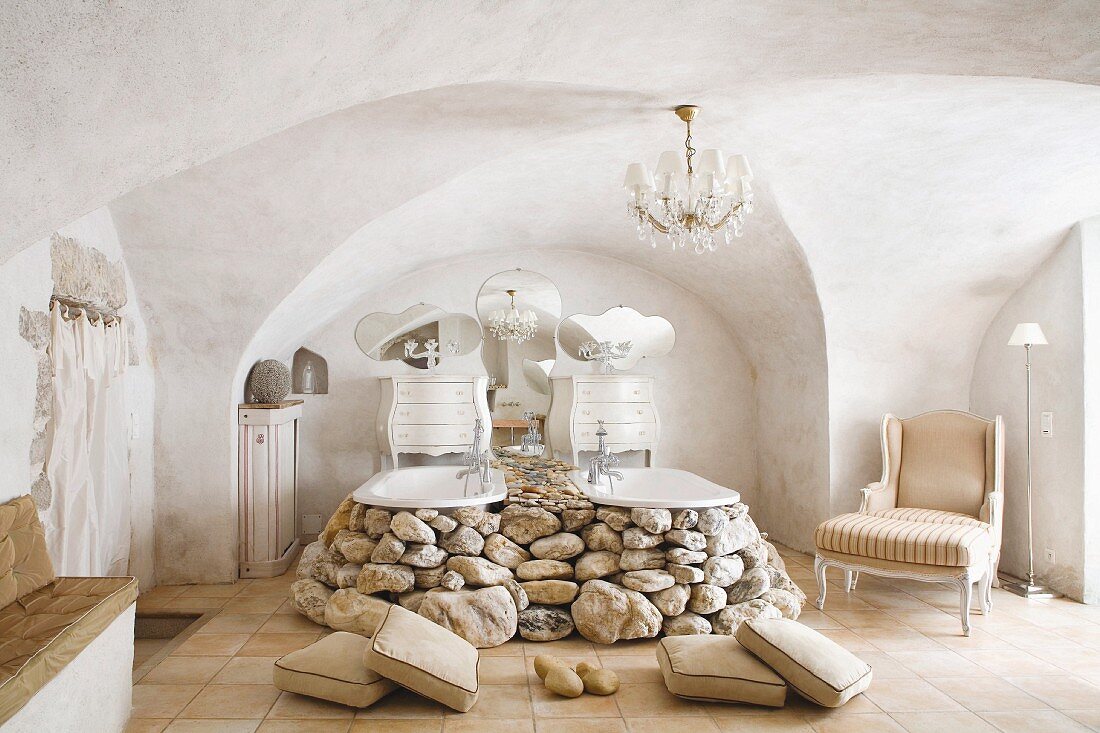 Two vintage bathtubs surrounded by boulders below chandelier hung from cross-vault