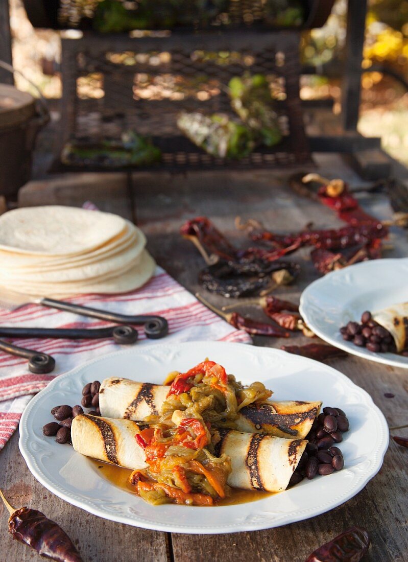 Black bean burritos and roasted chilli peppers on a wooden table outdoors