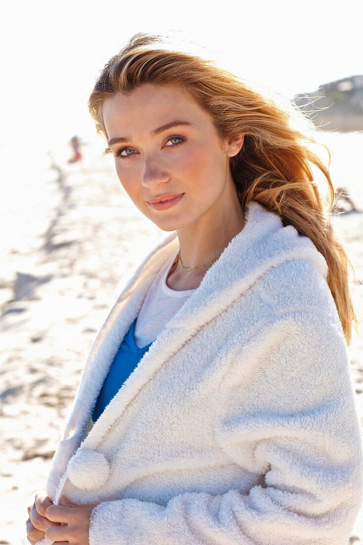 A young blonde woman on a beach wearing a white teddy fleece jacket