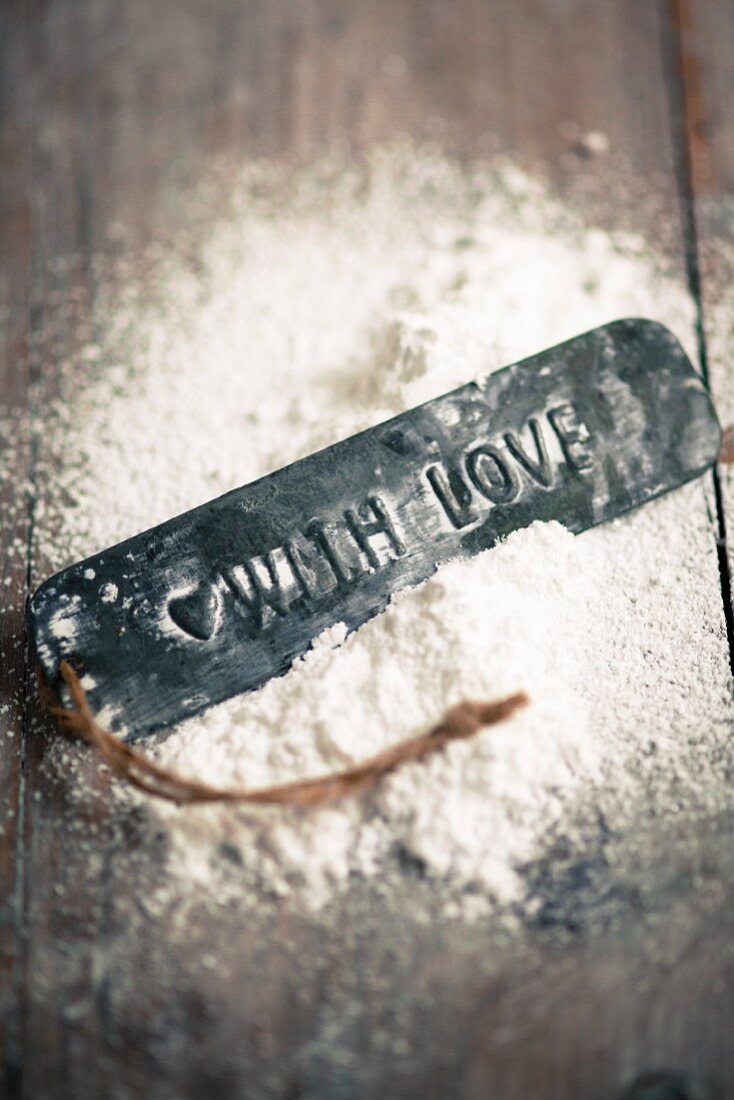 A gift tag with the words 'With Love' lying in a pile of flour