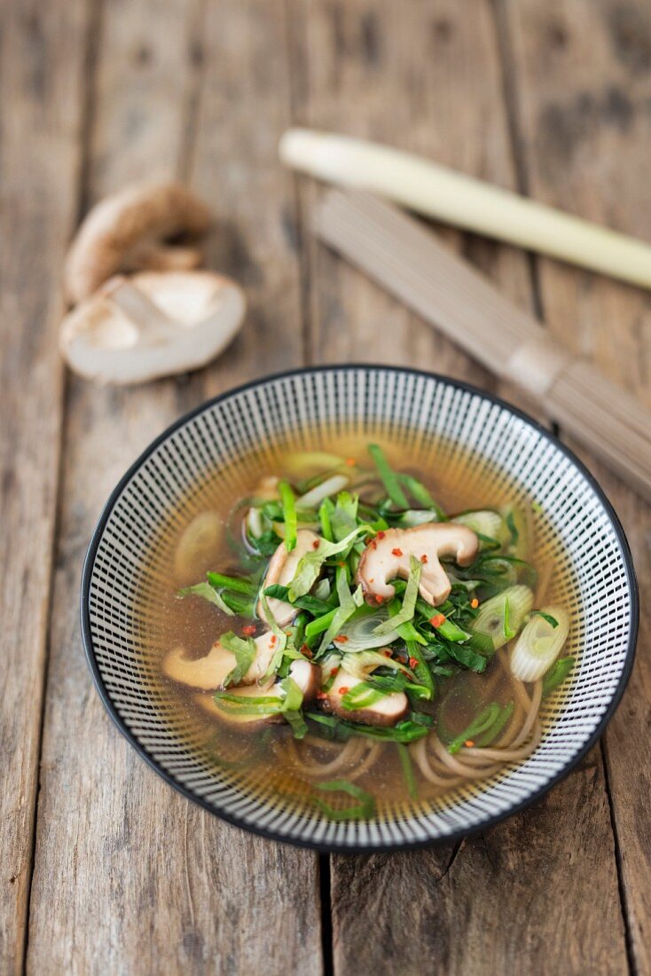 A bowl of Asian vegetable soup with Japanese buckwheat noodles on a wooden background