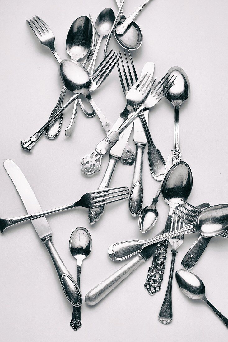 Various forks, knives and spoons on a white surface