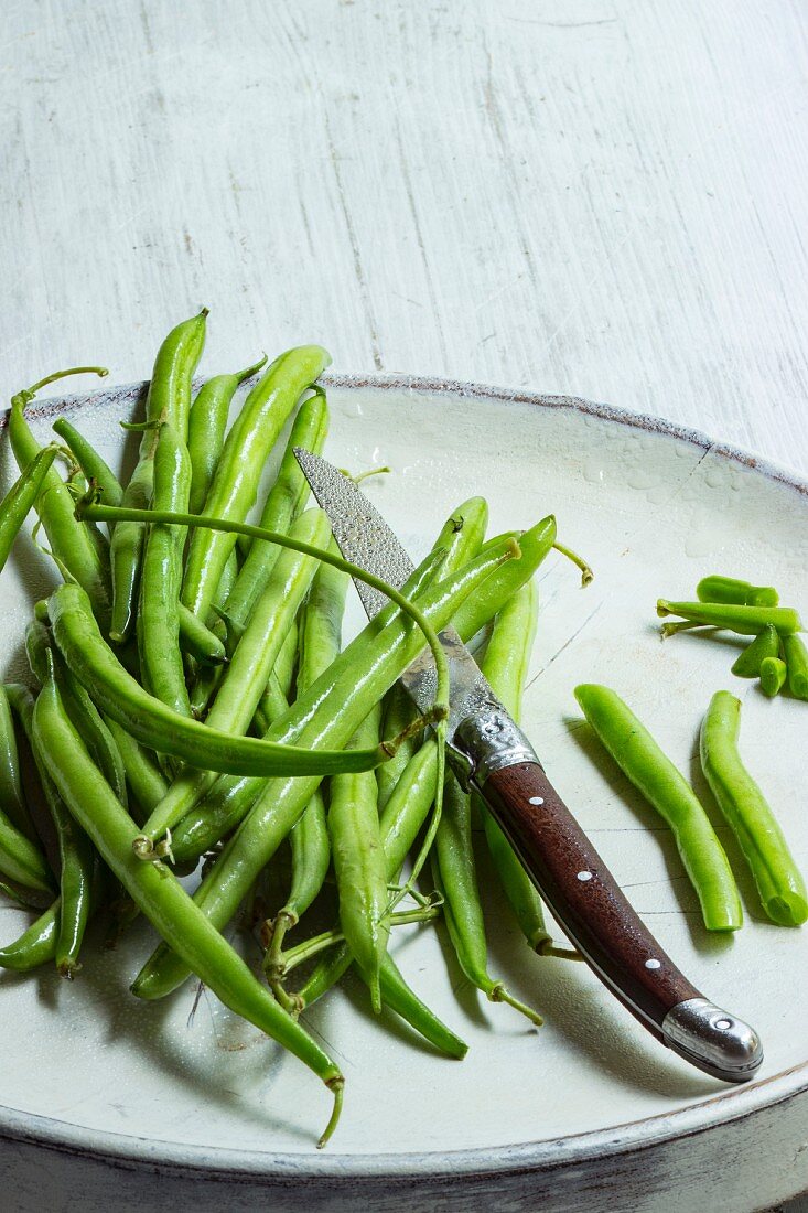 Fresh beans on a white plate with a knife being prepared