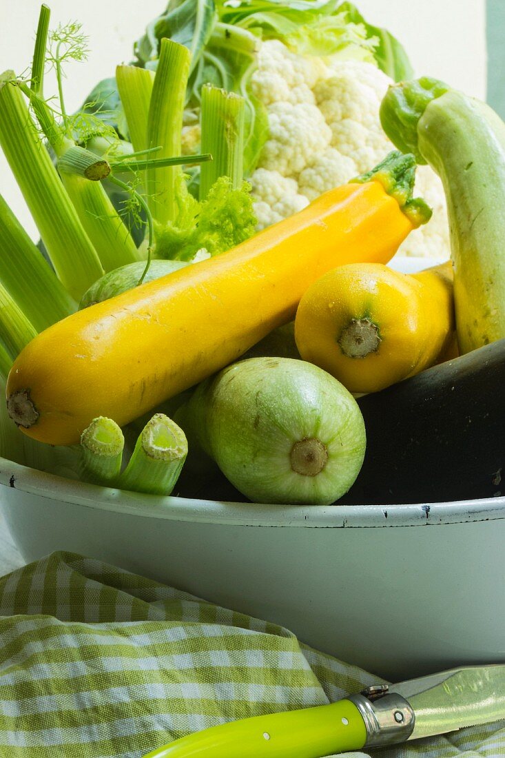 Fresh summer vegetables in a bowl with a tea towel and a knife