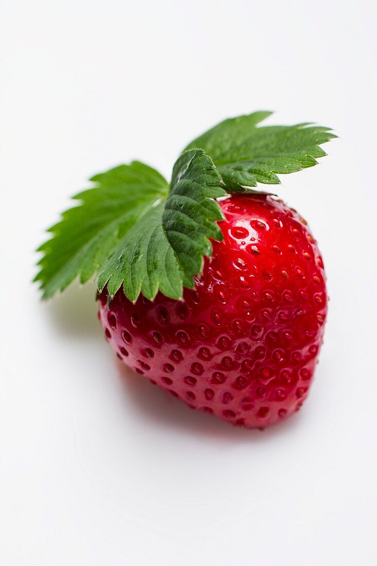 A strawberry with a leaf on a white surface