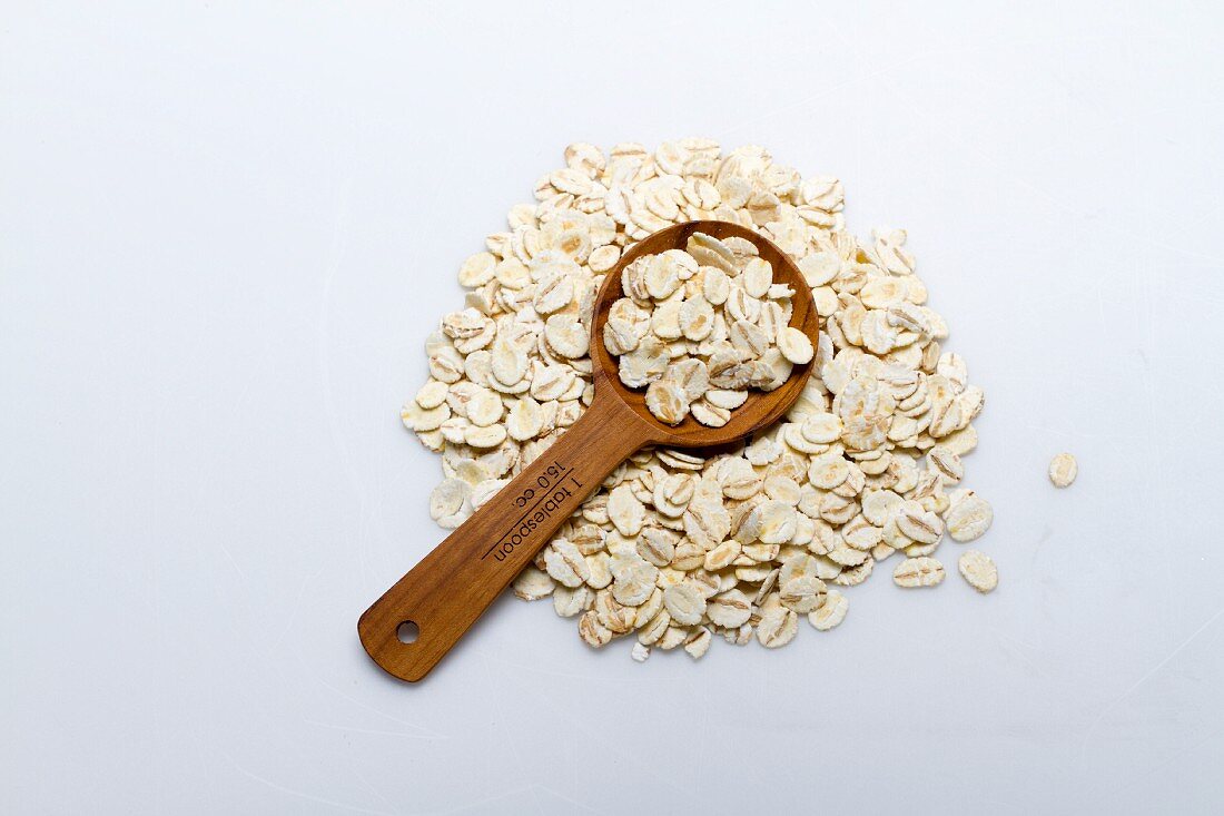 A pile of barley flakes with a wooden spoon on a white surface