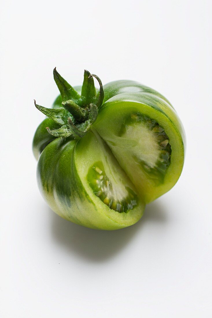 Eine grüne Tomate vor weißem Hintergrund, angeschnitten