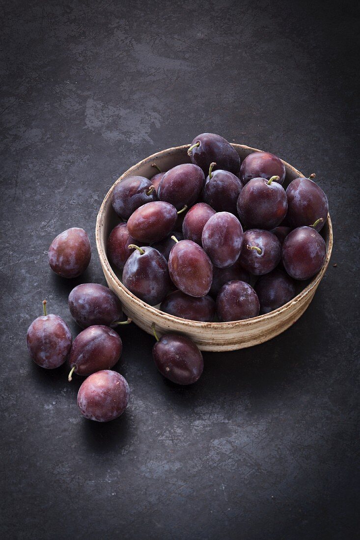 A bowl of fresh damsons on a black surface