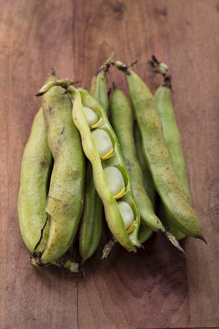 Broad beans in pods on a wooden surface