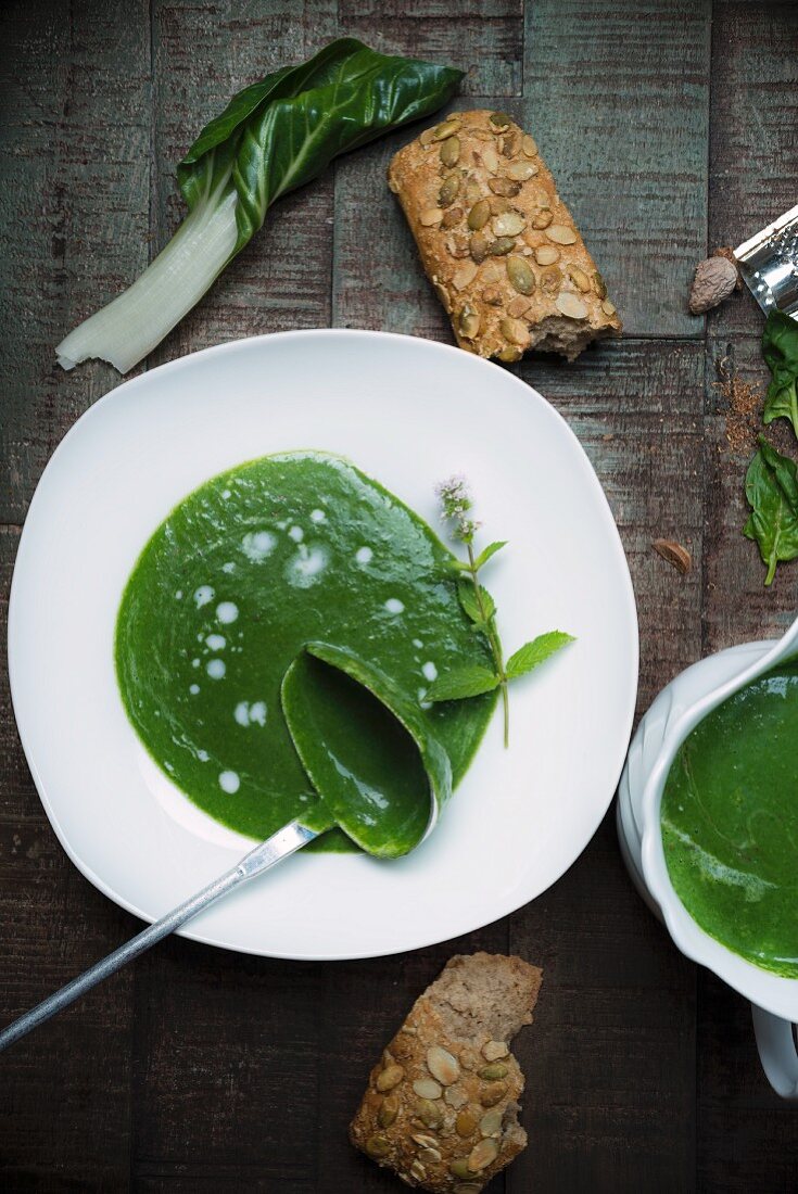 Spinach soup in a porcelain bowl on a dark wooden surface, nutmeg and a sunflower seed roll