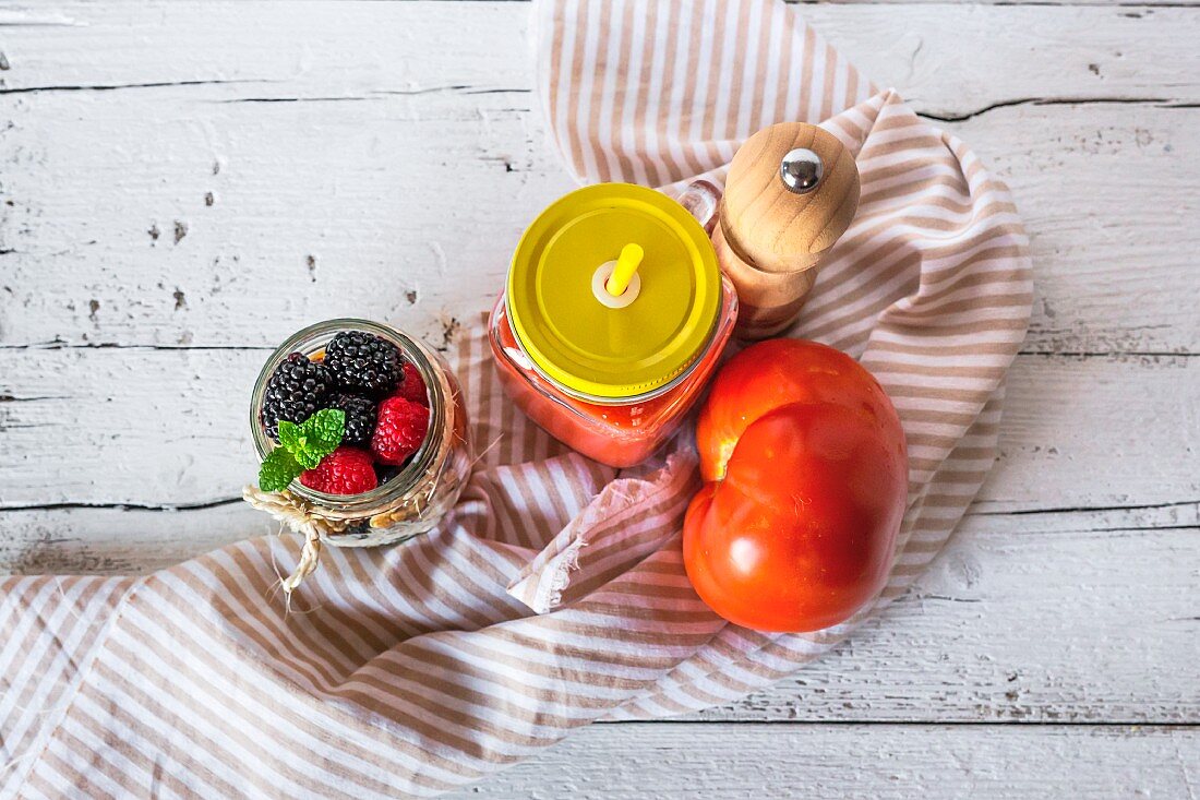 Cold tomato soup in a jar next to muesli with a jar of berries (seen from above)